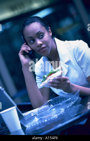 Ein Geschäft Frau sitzt außen versuchen, ihr Mittagessen zu Essen auf ihrem Computer arbeiten und alle zur gleichen Zeit auf einem Handy zu sprechen Stockfoto
