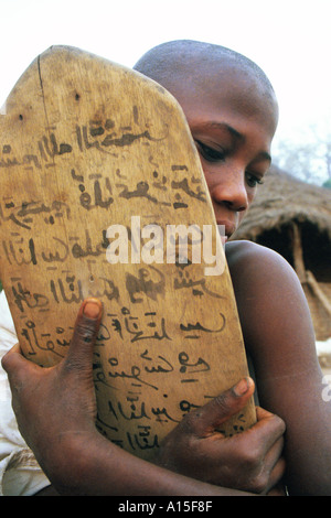 Ein Junge klammert sich an seinen hölzernen Studium Tablet um warm zu halten während der frühen Morgenstunden Studientagung in einem Fulani-Dorf im Westen Stockfoto