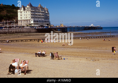 Touristen, die zum Sonnenbaden am Strand vor Llandudno pier Stockfoto