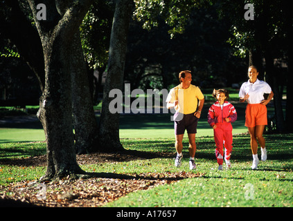 Attraktive Familie zusammen durch einen bewaldeten Park Joggen Stockfoto
