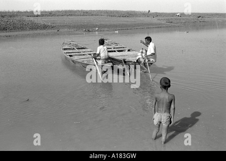 S/W von zwei Fischern, die in ihren Holzbooten arbeiten, beobachtet von einem kleinen Jungen auf einem Nebenfluss des Brahmaputra Flusses. Noapara, Bangladesch Stockfoto