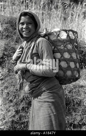 B/W-Porträt einer Bergfrau, die vom Markt nach Hause läuft, mit Vorrat in einem Korb auf dem Rücken. Uttarkashi, Garwhal Himal, N. Indien Stockfoto