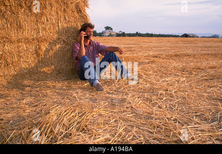 Junglandwirt mit zellulären Flip-Telefon auf Strohballen sitzend Stockfoto