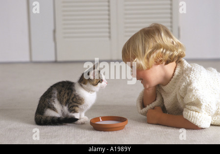 Blonde Mädchen betrachten ein Kätzchen, die Milch trinken ist Stockfoto