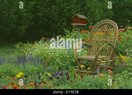 Verbogene willow handgefertigte Stuhl in einem leuchtend bunte home Blumengarten mit rotem Holz lackiert birdbox im Sommer Hinterhof, Missouri USA Stockfoto