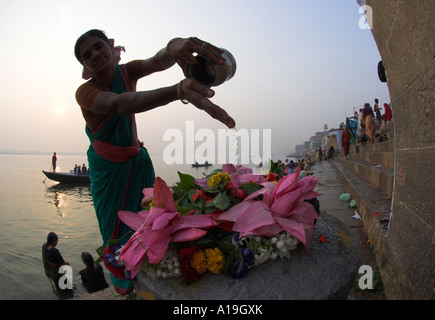 Uttar Pradesh Ganges in Indien Tal Varanassi Weitwinkel von Kedar Ghat bei Sonnenaufgang mit Frau gießt Wasser über Blumen auf eine Stockfoto