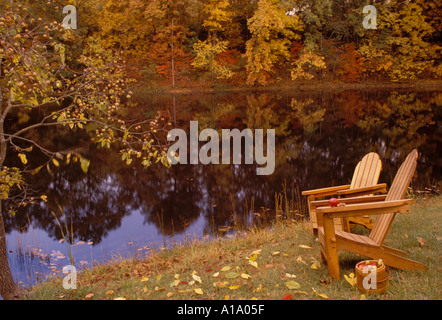 Zwei Zeder Adirondack Stühle an einem See mit Box von Äpfeln in farbigen Herbst Bäume im Wasser bei Jack Black Lake, Missouri USA widerspiegeln Stockfoto