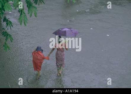 Indische Frau trägt einen Sari mit Regenschirm im Regen zu Fuß mit ihrem kleinen Kind ein Monsunzeit Stockfoto