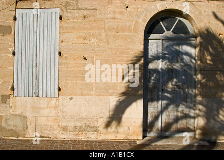 der weitläufige Schatten einer Palme fällt über eine Fassade und alte Gebäude und seine Haustür Stockfoto