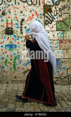 Eine Palästinenserin in traditioneller Kleidung kommt an einer mit Hajj-Gemälden geschmückten Wand im muslimischen Viertel der Altstadt von Jerusalem, Israel, vorbei Stockfoto