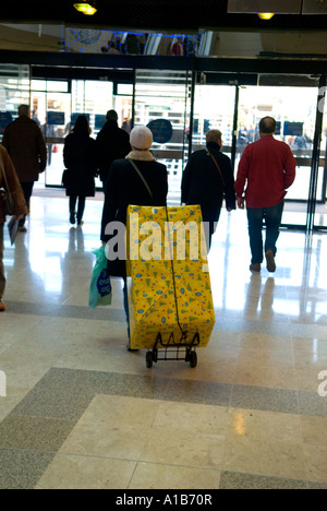 Eine Rückansicht eines weiblichen Shopper zu Fuß durch ein Einkaufszentrum mit einem sehr großen Geschenk auf einem Wagen Stockfoto