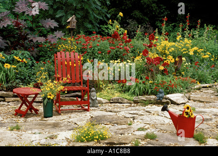 Red Garden: Rot bemalte Möbel auf Steinplatten Terrasse Garten mit passenden rote und gelbe Blüten Midwest USA Stockfoto