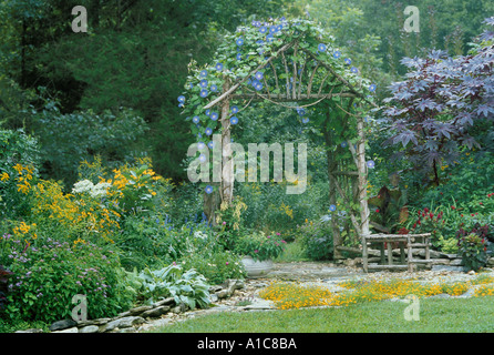 Handgemachte rustikale Zeder Laube mit blauen Prunkwinde Blumen von Steinplatten Terrasse im Blumengarten, Midwest USA Stockfoto