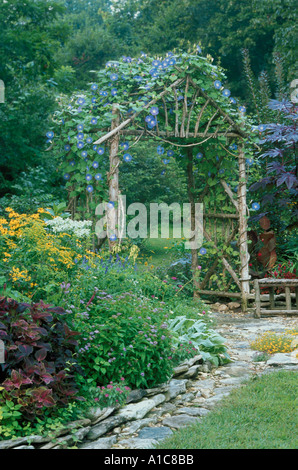 Rustikale Zeder Laube mit blauen Prunkwinde durch Steinplatten Terrasse im Blumengarten, in Missouri Stockfoto