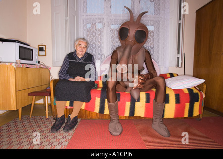 Alte Frau und ein hochgewachsener Mann in Moskito-Kostüm auf dem Bett sitzt Stockfoto