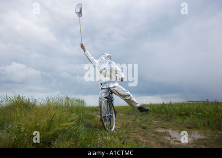 Mann in Feuerwehrmann Kostüm stretching, um mit dem Fahrrad in ein Sumpfgebiet Schmetterlinge zu fangen Stockfoto