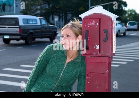 Junge, blonde Frau lehnte sich gegen ein Notruftelefon, das auf eine Stadt Bürgersteig Modell freigegeben ist Stockfoto