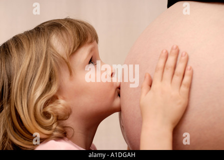 Kleines Mädchen, 4 Jahre alt, den Bauch der schwangeren Mutter küssen Stockfoto