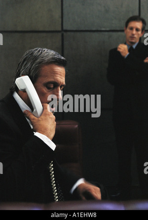 Geschäftsmann mit Festnetz-Telefon, zweite Geschäftsmann im Hintergrund Stockfoto