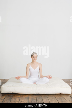 Junge Frau sitzt im Lotussitz auf Futon-Matratze Stockfoto