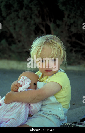 kleine blonde Mädchen sitzen außen hält ihr Babypuppe Stockfoto