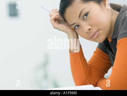 Junge Frau stützte sich auf Ellbogen, Stift in der hand halten Stockfoto