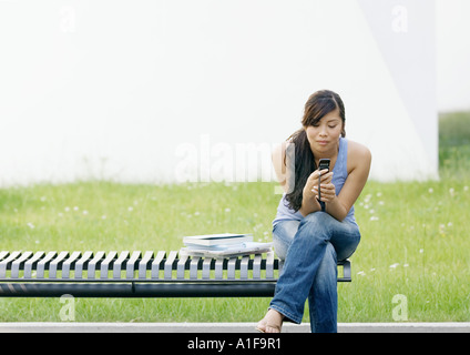 Junge Frau sitzt am Ende der Bank Blick auf Handy Stockfoto