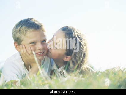 Jungen und Mädchen liegen auf dem Rasen, Mädchen, jungen auf die Wange küssen Stockfoto