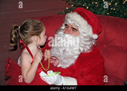 Kind sitzt auf Santa Claus Schoß, ihm zu sagen, welche Geschenke sie zu Weihnachten wünschen Stockfoto