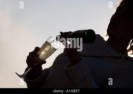 Eine junge Frau, die sprudelnden Champagner in Longdrinkglas aus kleinen Champagner-Flasche gießen. Silouette gegen Sonnenlicht. Stockfoto