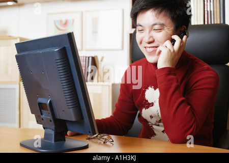 Nahaufnahme eines Geschäftsmannes sitzt vor einem Computer-Monitor mit dem Handy telefonieren Stockfoto