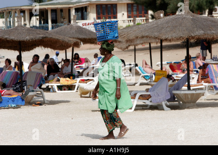 Frau Obstverkäufer in traditioneller Kleidung trägt Ananas im Korb auf Kopf The Cape Beach Bakau Gambia Stockfoto