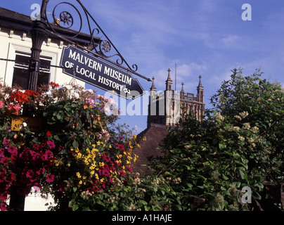 Eine Straßenlaterne und ein Zeichen für das örtliche Museum mit seinen hängenden Körben von Blumen in der Nähe von der Kirche in Great Malvern Stockfoto