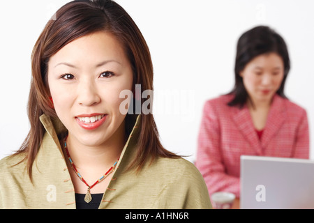 Porträt von eine Geschäftsfrau, die mit einem anderen Geschäftsfrau mit einem Laptop hinter ihr Lächeln Stockfoto