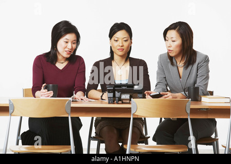 Drei Geschäftsfrauen sitzen auf Stühlen, Blick auf das Telefon Stockfoto