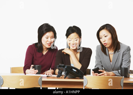 Drei Geschäftsfrauen sitzen auf Stühlen, Blick auf das Telefon Stockfoto