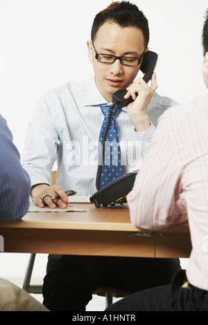 Nahaufnahme eines Geschäftsmannes mit zwei Geschäftsleute, die vor ihm saß am Telefon sprechen Stockfoto