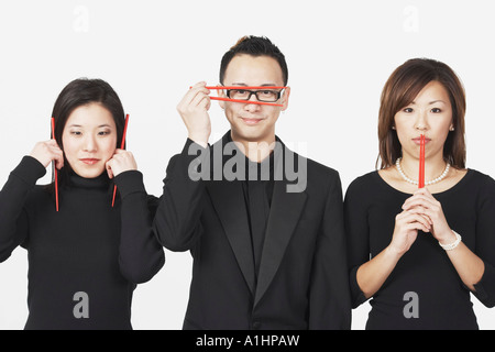 Zwei junge Frauen und ein junger Mann, gestikulieren sprechen nichts Böses, nichts Böses hören, sehen, nichts Böses mit Stäbchen Stockfoto