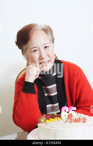 Portrait einer älteren Frau sitzt vor einem Geburtstag Kuchen lächelnd Stockfoto