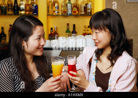 Zwei junge Frauen, die sitzen in einer Bar Zähler erhöhen einen toast Stockfoto