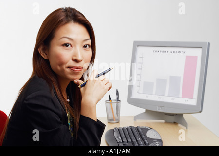 Porträt einer Geschäftsfrau vor einem Computer sitzen und halten Sie einen Stift Stockfoto