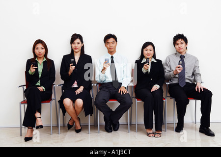 Porträt von zwei Geschäftsleuten und drei Geschäftsfrauen beisammen sitzen und halten Handys Stockfoto