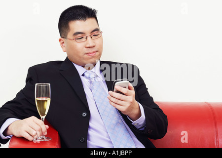 Nahaufnahme eines Geschäftsmannes hält ein Champagnerglas und den Betrieb eines Mobiltelefons Stockfoto