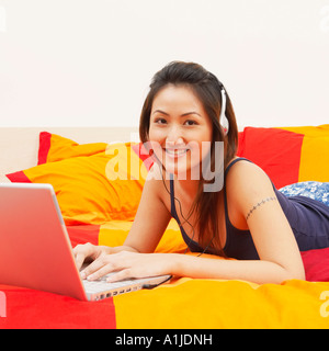 Porträt einer jungen Frau auf dem Bett liegend und mit einem laptop Stockfoto