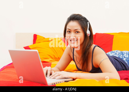 Porträt einer jungen Frau auf dem Bett liegend und mit einem laptop Stockfoto