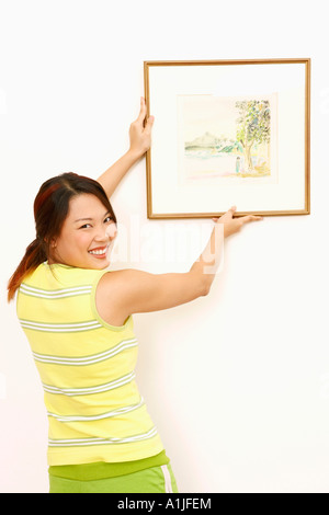 Porträt einer jungen Frau einen Bilderrahmen an der Wand hängen und lächelnd Stockfoto