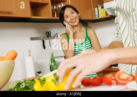 Mitte Schnittansicht von einem Mann Schneiden von Gemüse mit einer jungen Frau telefonieren mit einem Handy in der Küche Stockfoto