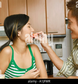 Nahaufnahme eines jungen Mannes Fütterung eine Scheibe Tomate, einer jungen Frau an einer Küchentheke Stockfoto