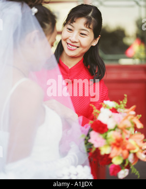 Junge Frau mit Blick auf eine andere Frau im Hochzeitskleid und lächelnd Stockfoto