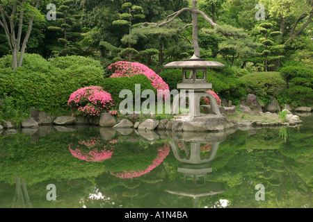 Steinlaterne in einem üppigen grünen traditionellen japanischen Garten mit leuchtend rosa Blüten auf dem Gelände des Osaka Schlosses Japan Asien Stockfoto